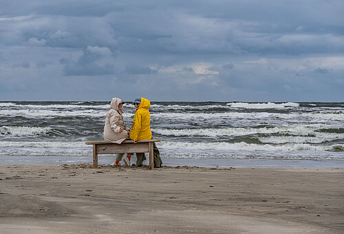 Herbsturlaub auf Juist - zwei Personen in Jacken am Strand auf Juist vor den Wellen an der Wasserkante